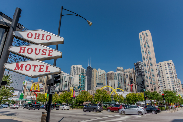 Red and white sign for Ohio House Motel with cars and buildings in background